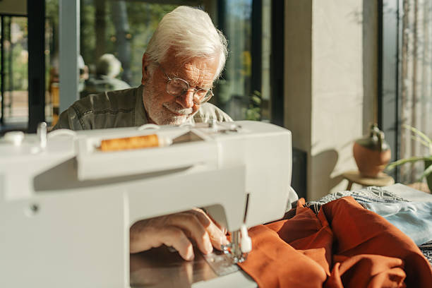 istock Senior man sewing fabric on a sewing machine 2212729130