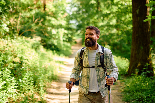 istock Smiling hiker walking in forest using trekking poles and backpack 2212731545