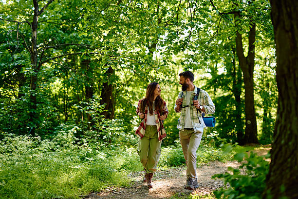 Young couple smiling and enjoying each other's company while hiking along a scenic forest trail, sharing laughter and conversation under the warm summer sun