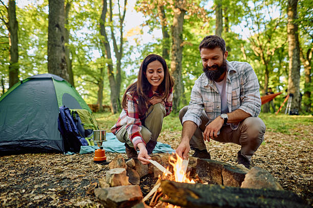 istock Couple camping and lighting bonfire in forest next to tent 2212736005