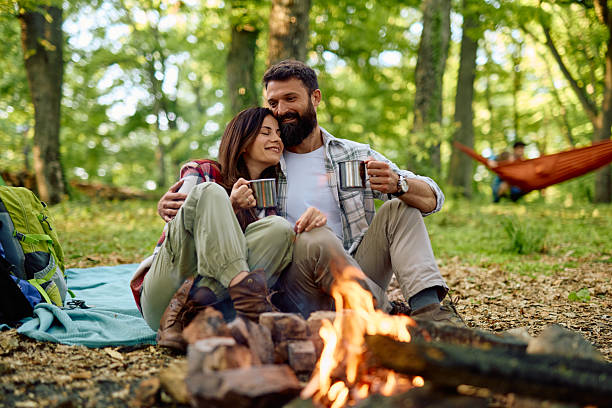 istock Couple camping and drinking hot beverages near campfire in the forest 2212736611