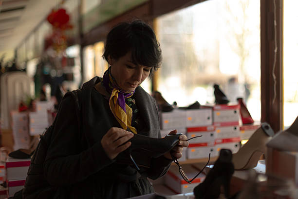 A woman with black hair is browsing through a selection of shoes displayed in an upscale store, evaluating her options thoughtfully