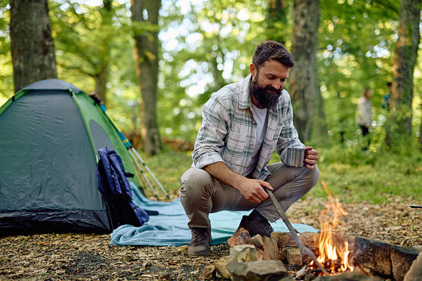 istock Camper drinking coffee and adjusting campfire flames in the forest 2212738966