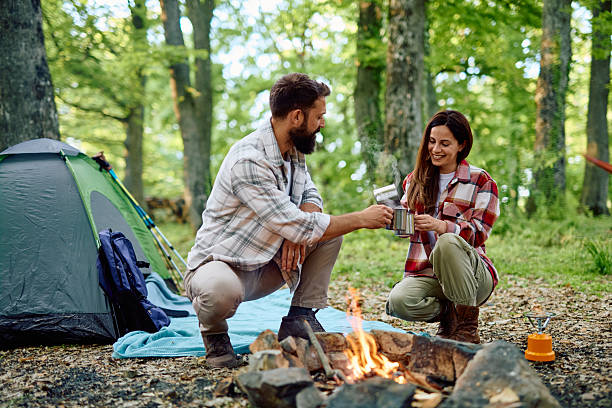 istock Couple camping and drinking hot beverages by campfire in forest 2212739170