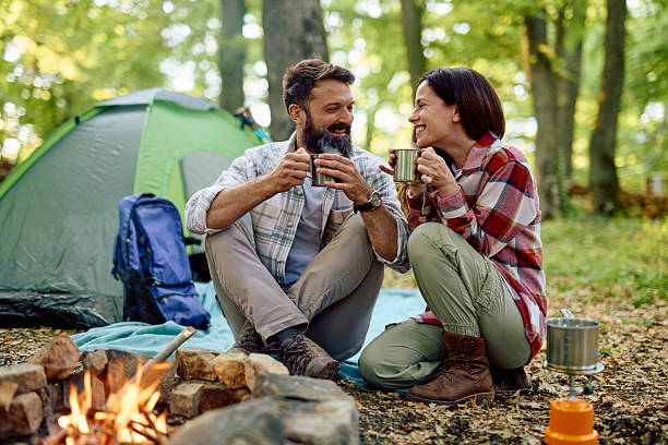 istock Couple camping and drinking hot beverages near campfire in forest 2212739732
