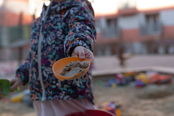 A joyful child offers soft sand from a colorful bowl, showcasing playful moments in a lively playground at sunset