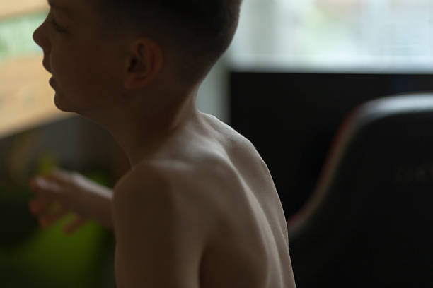 In a softly illuminated indoor space, a young boy with an exposed back is captured in a tranquil moment