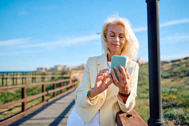 istock Elegant senior businesswoman using smartphone on beach boardwalk 2212746425