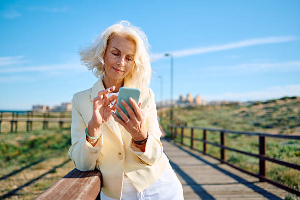 istock Elegant senior businesswoman using smartphone on beach boardwalk 2212746445