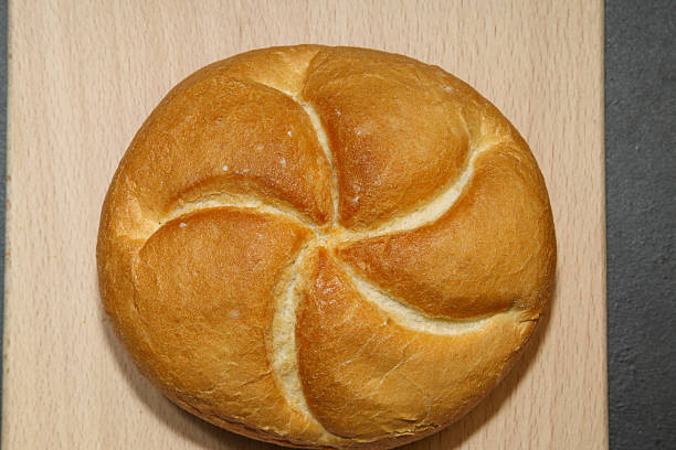 Golden round bread roll with a five-part swirl pattern on a light fabric background. Crisp crust and artisan texture, photographed from above.