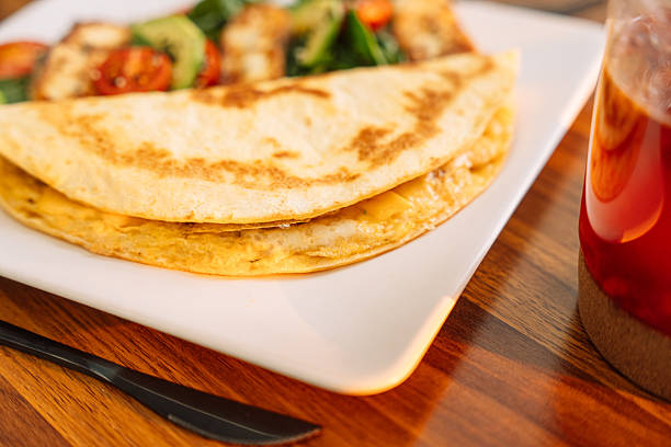 Top view of a quesadilla served with guacamole, accompanied by various salsas and a refreshing drink on a rustic wooden table