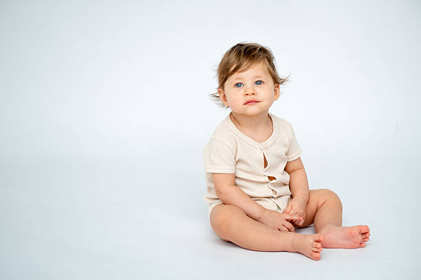 istock A baby boy is sitting on a white isolated background with a place for text in light clothes. A small happy child, space for text 2212756934