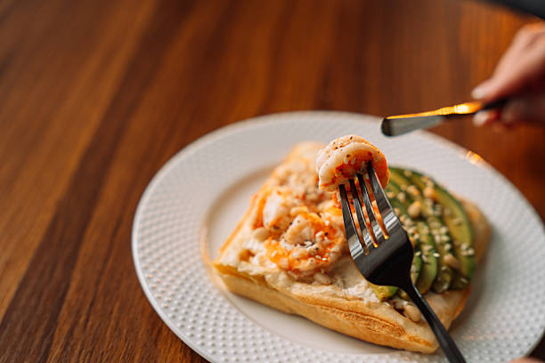 Shrimp waffles on a fork at a wooden table.