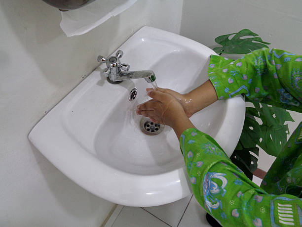 Stock photo showing a modern white bathroom suite with a bath featuring a chrome mixer tap being used to fill the tub with water. The bathroom has been tiled with marble wall tiles.