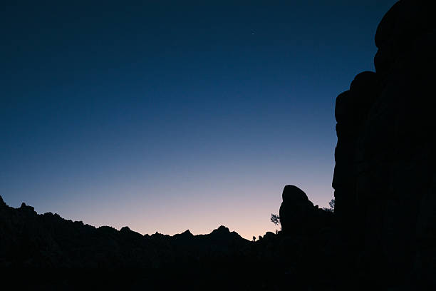 A dramatic granite spire stands silhouetted against the deep blue hues of twilight in Joshua Tree National Park. The scene captures the quiet majesty of the desert landscape at blue hour, emphasizing natural textures, timeless stillness, and the serene beauty of protected wilderness.