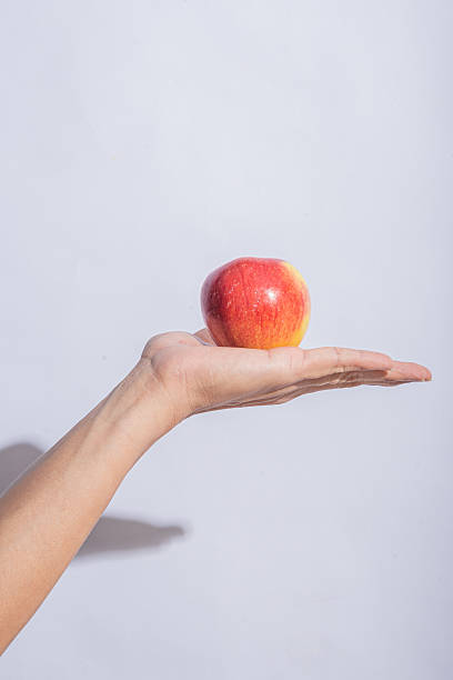 istock A red apple resting on an open palm against a clean light gray background, emphasizing the fruit's fresh texture and vibrant color 2212769463