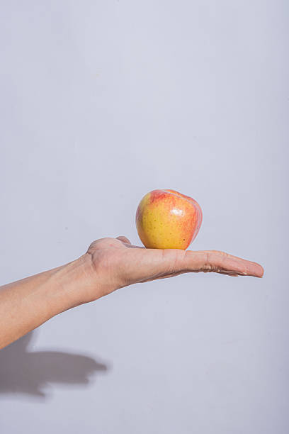 istock A red apple resting on an open palm against a clean light gray background, emphasizing the fruit's fresh texture and vibrant color 2212769644