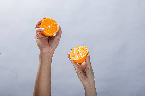 istock Two hands holding fresh orange halves against a plain light background, showing juicy citrus texture, vibrant color, and a healthy, natural fruit presentation in midair pose 2212772433