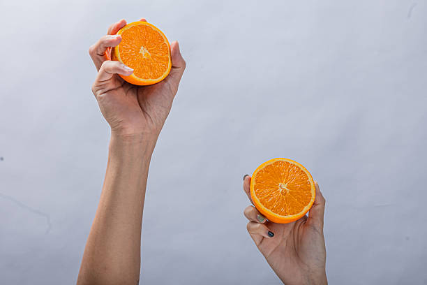 istock Two hands holding fresh orange halves against a plain light background, showing juicy citrus texture, vibrant color, and a healthy, natural fruit presentation in midair pose 2212772447