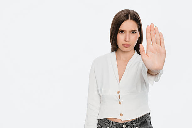 istock Woman in White Shirt Exhibiting Stop Gesture with Serious Expression 2212772702