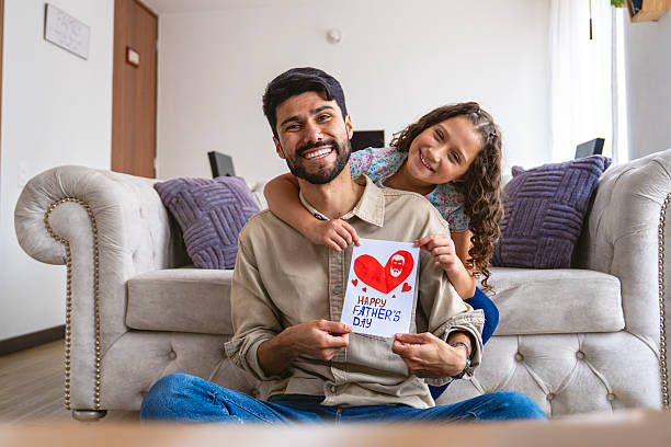 Happy moment between father and daughter sitting on the couch, sharing a handmade Father's Day card at home.