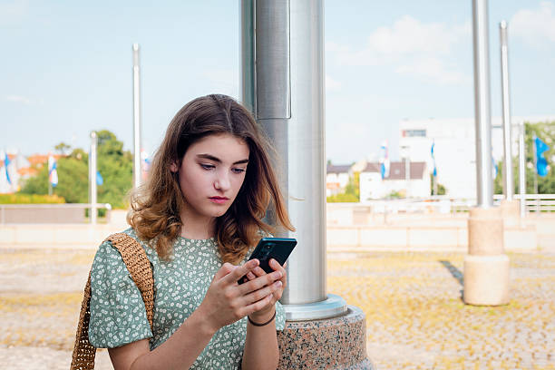 istock Young girl using smartphone outdoors on sunny day in modern city square 2212774790