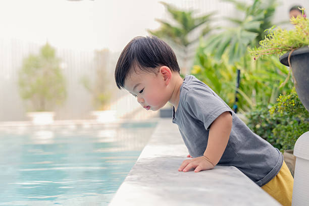 istock fun and cheerful Asian toddler child boy  sit over poolside and try to explore watching into water in summertime vacation playful moment 2212776567