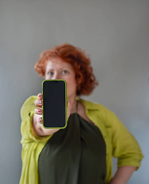 istock Digital display presentation. Redhead woman with chartreuse cardigan shows smartphone screen. 2212777029