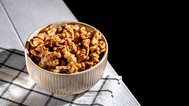 istock Shelled walnuts resting in a bowl on a checkered tablecloth create an inviting scene, complemented by a dark background that enhances the natural textures and colors 2212777515