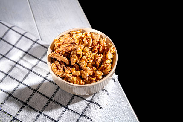istock Shelled walnuts resting in a bowl on a checkered tablecloth create an inviting scene, complemented by a dark background that enhances the natural textures and colors 2212777815