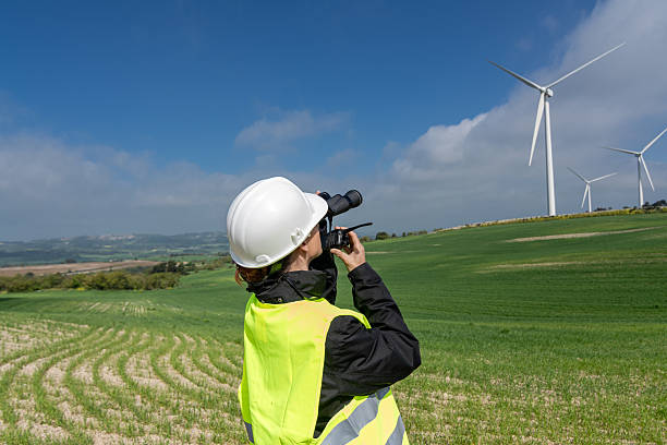 istock Female engineer inspecting wind turbines with binoculars in green field 2212779723