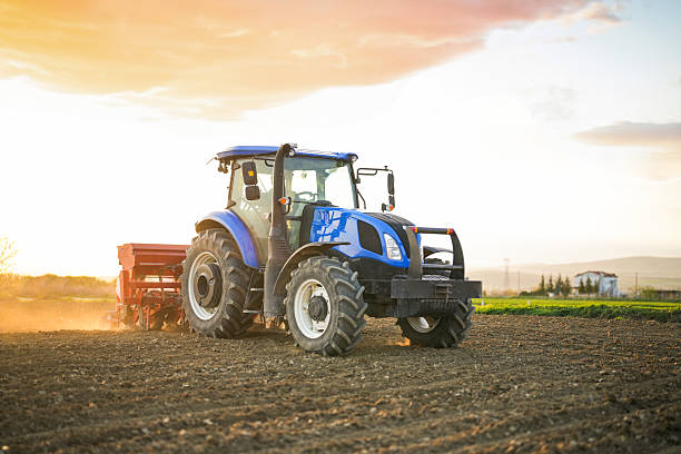 A farmer sowing seeds with a tractor and seed drill in a field at sunset