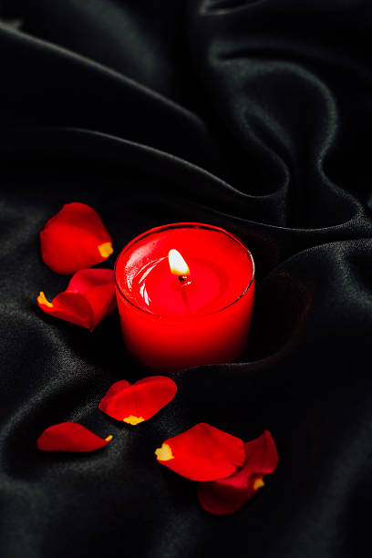 istock Red candle surrounded by rose petals on black silk fabric in soft light setting ambiance 2212783749