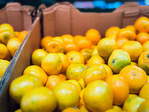 A detailed view of a corrugated cardboard box completely filled with fresh oranges, ready for sale.