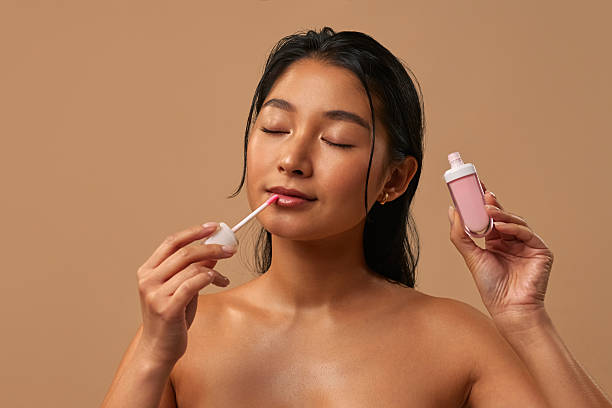 istock Asian woman with lip gloss on a beige background 2212787583