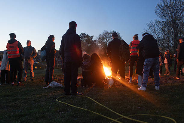 Silhouettes of people surrounding a glowing bonfire at dusk, part of the traditional Swedish Valborg (Walpurgis Night) festivities marking the start of spring. Shot in Edsviken in Sollentuna, Sweden.