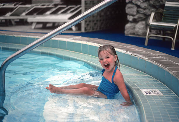 Portrait of a young girl in a vibrant swimsuit swimming in a pool on a sunny day. She enjoys the refreshing water and summer fun.