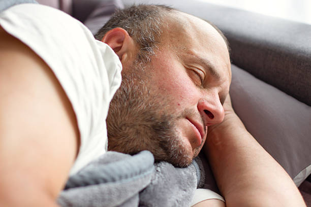 Tired and exhausted middle-aged man sleeping under a gray blanket.