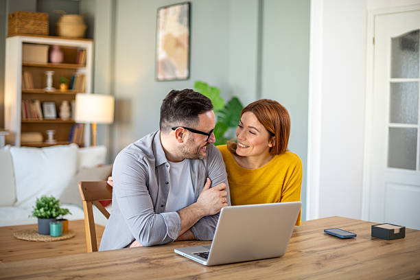 istock Happy couple smiling and looking at each other while using laptop at home 2212808096