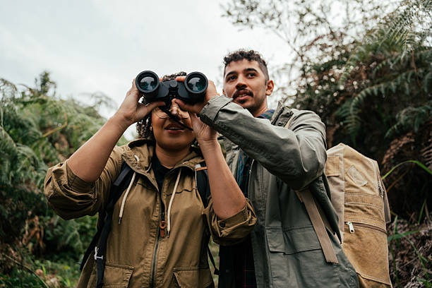 istock Young couple hiking in the forest and watching birds through binoculars 2212808256