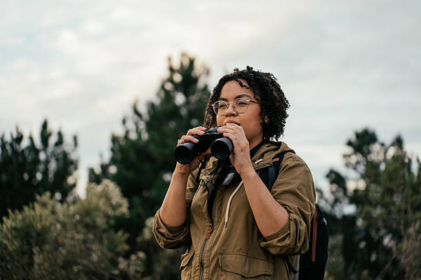 Young woman watching birds with binoculars in the forest