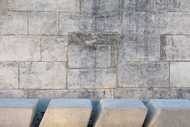 Background of large rectangular stone blocks wall with varied coloration and natural texture with angled concrete blocks across the bottom edge.