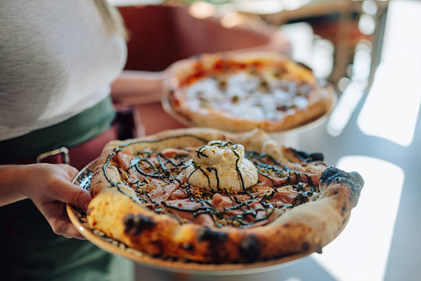 Waitress is holding two freshly baked pizzas, one topped with burrata cheese and mortadella, ready to be served in a restaurant