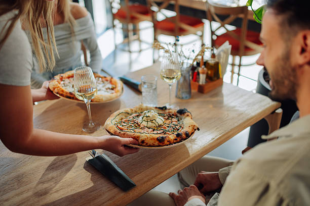 istock Waitress serving pizza to customers in restaurant 2212809216
