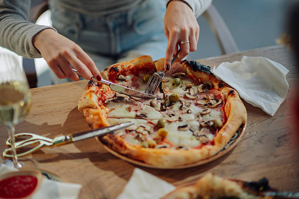 Woman enjoying a delicious pizza with mushrooms, ham, and olives, cutting a slice with knife and fork in a pizzeria
