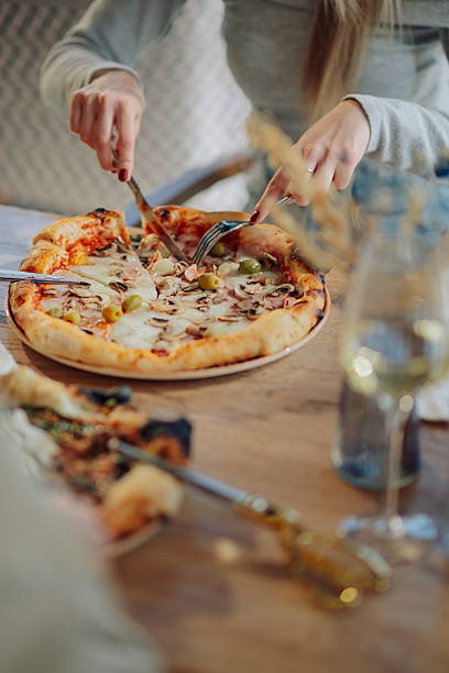 istock Woman cutting pizza with knife and fork in restaurant 2212809228