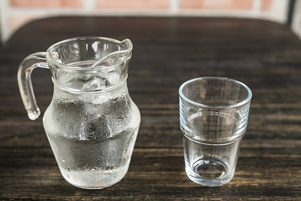 Glass and jug with water on wooden table.