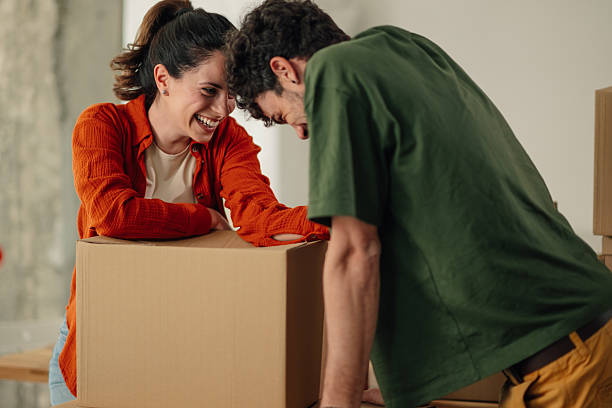 istock Happy couple laughing while leaning on cardboard box in new home 2212811403
