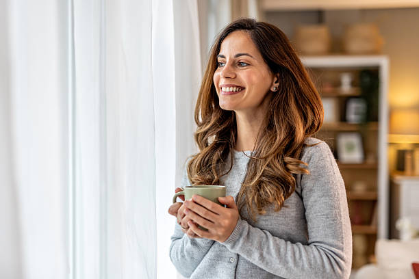 istock Woman Smiling While Holding Mug in Bright and Cozy Home Interior 2212812167