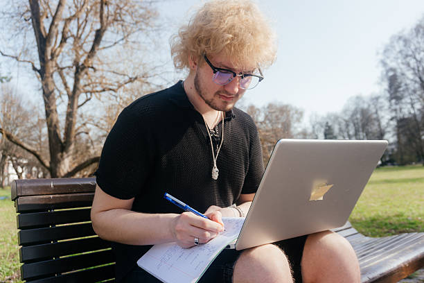 istock A focused student works outdoors on a laptop and takes notes while sitting alone on a park bench on a sunny day 2212812237